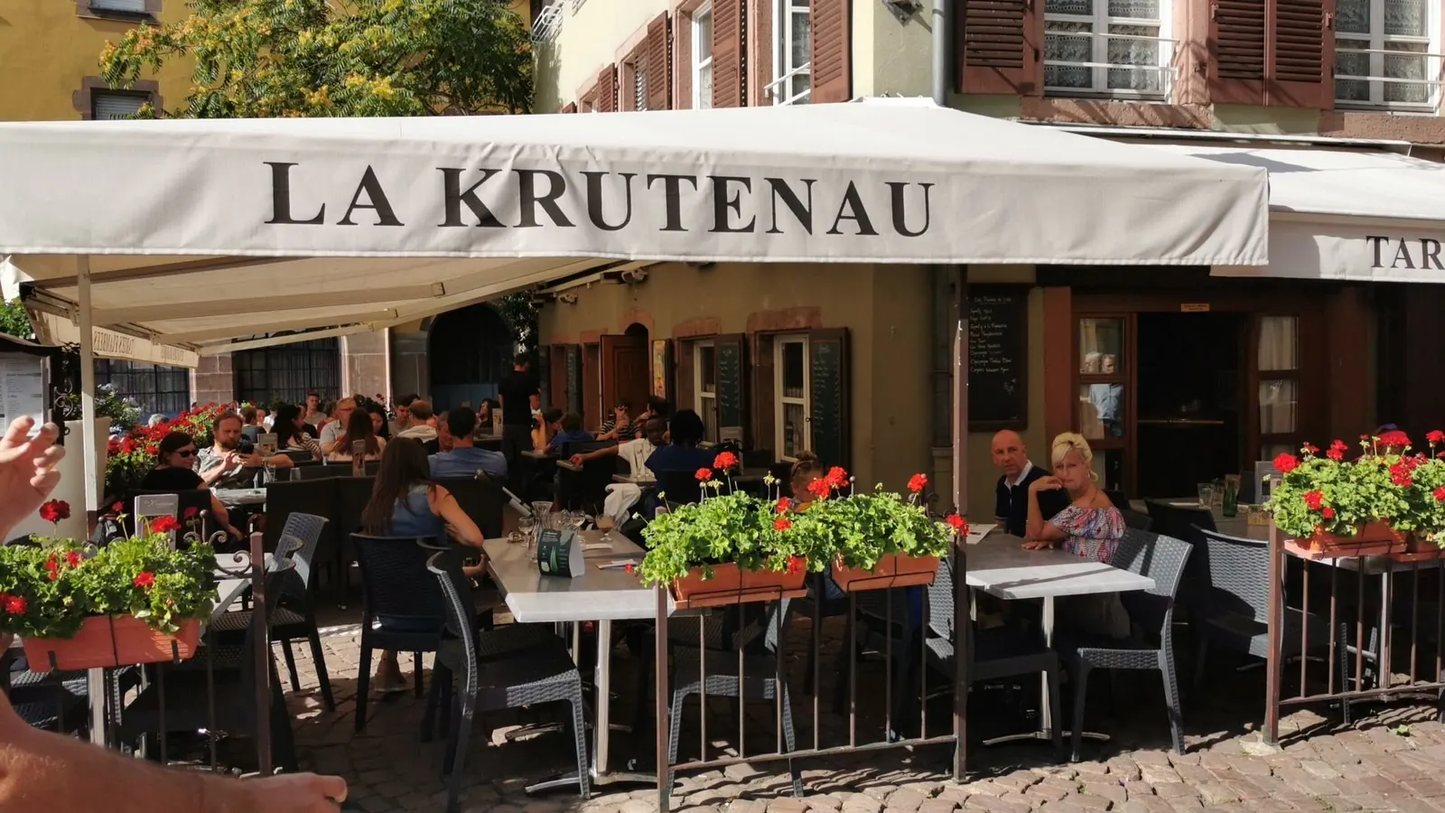 La terrasse sous l'auvent « La Krutenau », géraniums rouges et tables pleines